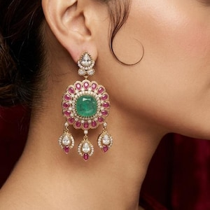 Peut inclure: Boucles d'oreilles pendantes dorées ornées d'une pierre centrale émeraude, entourée de rubis. Le design floral comprend trois pendentifs en forme de goutte avec des pierres blanches et des détails rubis. Bijou de luxe.