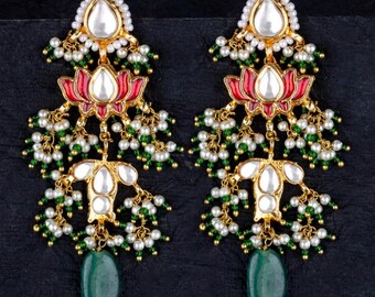 May include: A pair of gold-toned earrings with a floral design. Each earring features a teardrop-shaped green stone, white pearl accents, and red and white floral elements. The earrings have a layered design.