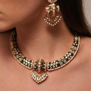 May include: An ornate gold necklace and matching earrings set. The necklace features a black and green enamel design with white gemstone accents and a central pendant. The earrings mirror the necklace's design, creating a cohesive jewelry set.
