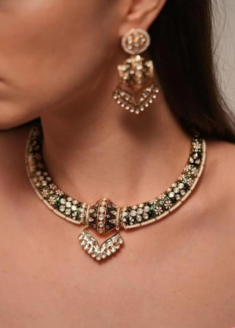 May include: An ornate gold necklace and matching earrings set. The necklace features a black and green enamel design with white gemstone accents and a central pendant. The earrings mirror the necklace's design, creating a cohesive jewelry set.