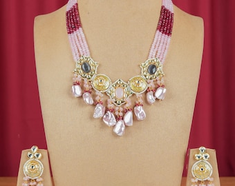 May include: A pink and red beaded necklace with a gold and pearl pendant. The necklace is paired with matching earrings.