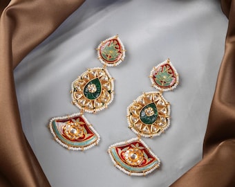 May include: A pair of gold earrings with red, green, and blue enamel detailing. The earrings feature a teardrop shape with a round center piece and a fan-shaped bottom.