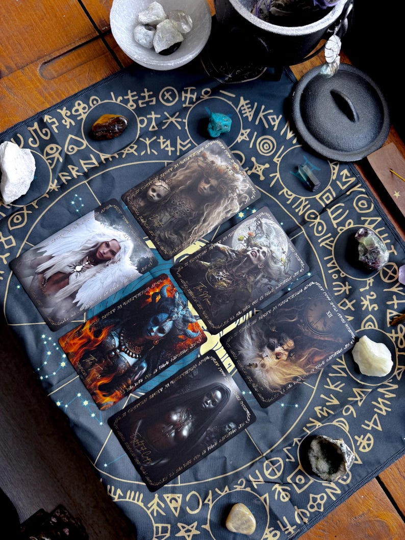 May include: A collection of tarot cards with fantasy art, arranged on a dark blue mat with gold symbols. The cards feature images of mystical figures and scenes. Various crystals and a small cauldron are also present, creating a spiritual theme.
