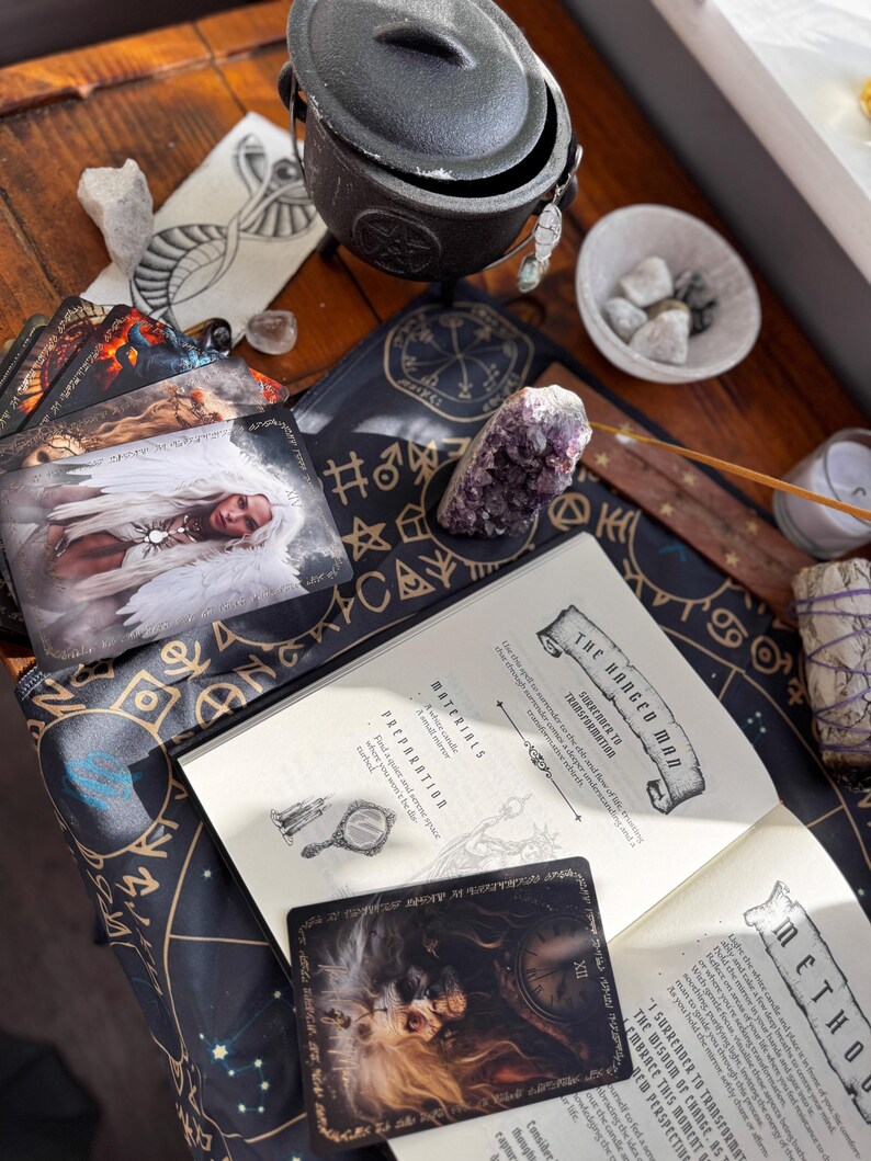 May include: An assortment of spiritual tools on a wooden surface. Includes a black cauldron, tarot cards, a book with the title "The Hanged Man", crystals, and a smudge stick. The cards feature angel imagery and the book has text.
