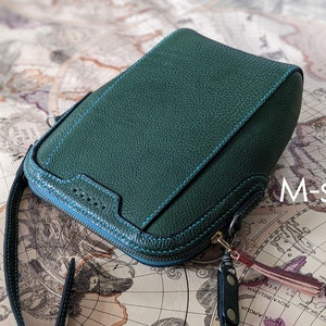 May include: A dark green leather bag with a zipper closure and a blue zipper pull. The bag has a black strap and a small metal tag with a brown tassel. The bag is labeled "M-size".