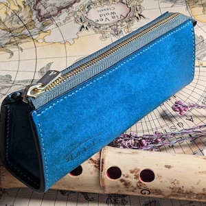 Op de afbeelding: Een blauwe leren etui met rits en de tekst "Leather Goods Italy" en "Lavori Artigianali" gegraveerd op de voorkant.