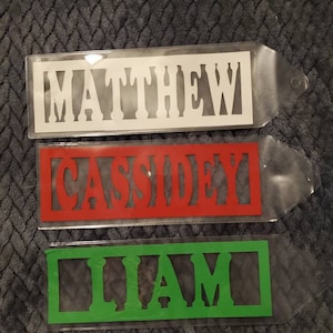 May include: Three clear plastic name tags with white, red, and green lettering. The names are "MATTHEW", "CASSIDEY", and "LIAM".
