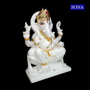 May include: White marble statue of Ganesha, the Hindu god of wisdom and prosperity, with a gold crown and accents. The statue is sitting on a lotus base with a small mouse at its feet.