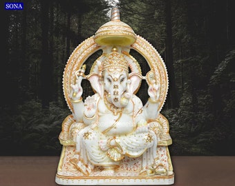 Op de afbeelding: Wit marmeren beeld van Ganesha, de hindoeïstische god van wijsheid en voorspoed, zittend op een troon met een gouden halo en kroon. Het beeld is versierd met ingewikkelde details en gouden accenten.