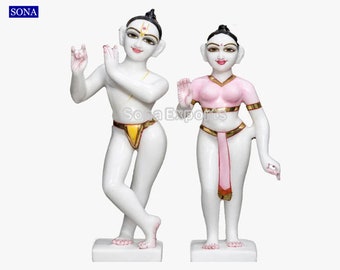 May include: White marble statue of a couple, the male figure is holding a flute and the female figure is wearing a pink garment.