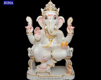Op de afbeelding: Een witte marmeren beeld van de hindoeïstische god Ganesha, zittend op een troon. Het beeld heeft gouden accenten, een kroon en een kleine muis aan de basis. De tekst "Sona Exports" is zichtbaar.