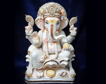 May include: White marble statue of Ganesha, the Hindu god of wisdom and prosperity. The statue is intricately carved with gold accents and features a crown, a trunk, and a large belly. The statue is sitting on a lotus base.