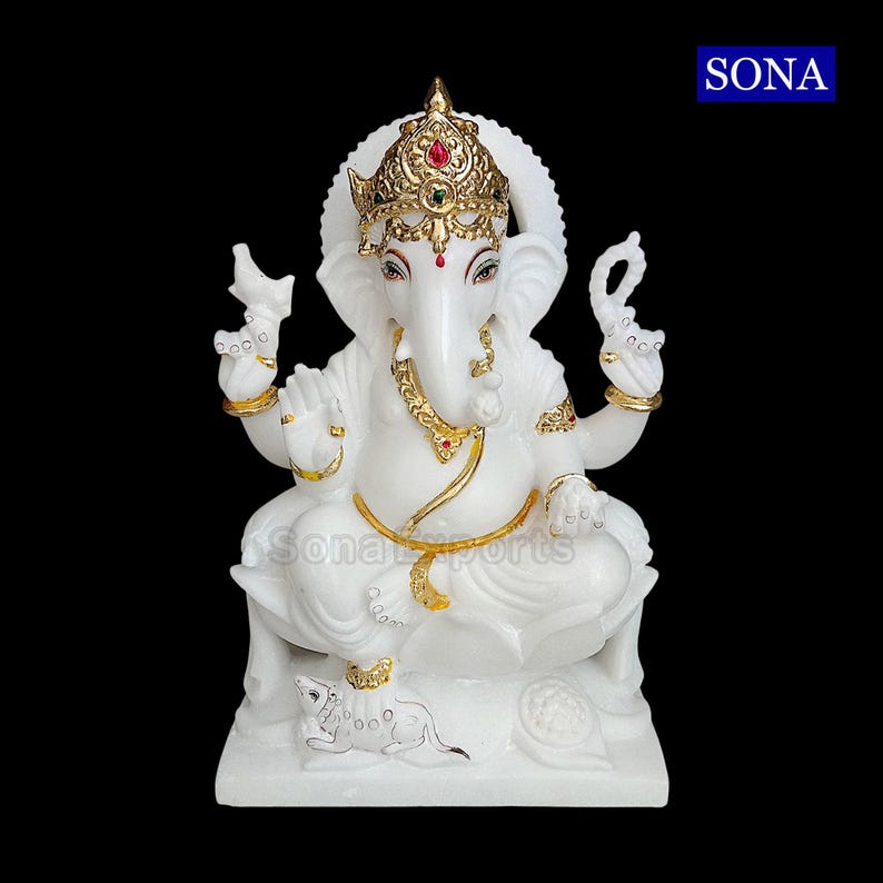 May include: White marble statue of Ganesha, the Hindu god of wisdom and prosperity. The statue is decorated with gold paint and features a crown, a trunk, and a mouse. The statue is sitting on a base with a lotus flower design.