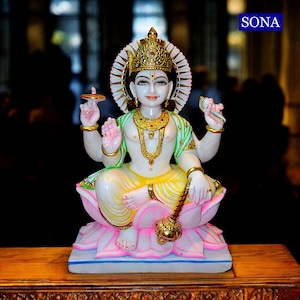 May include: A white marble statue of a deity seated on a pink lotus flower. The figure wears a gold crown, jewelry, and a green and yellow garment. The statue has multiple arms and is holding various objects. The word "SONA" is in the upper right corner.