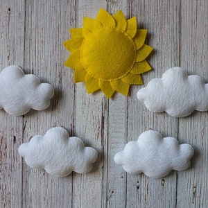 May include: A yellow felt sun with a white felt border and five white felt clouds on a wood background.
