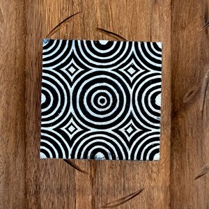 May include: A black and white wooden block with a repeating pattern of concentric circles and diamonds. The block is on a wooden surface.