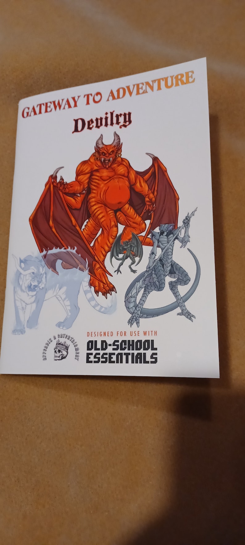 May include: A white booklet with the title "Gateway to Adventure: Devilry" and a colorful illustration of a red devil, a grey dragon, and a white wolf. The booklet is designed for use with "Old-School Essentials".