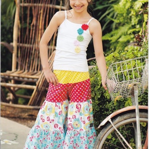 May include: A young girl wearing a white tank top adorned with colorful flower appliqués and patterned gaucho pants. The pants feature red, yellow, and blue floral patterns. The image includes the text "Pink Fig PATTERNS" and "Lilous market day gaucho's no.31".