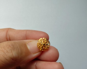 May include: A small, round, gold-colored stud earring featuring an intricate, openwork filigree design with a textured, granular surface. The piece has a domed, spherical shape and a metallic finish, showcasing detailed metalwork throughout its structure.