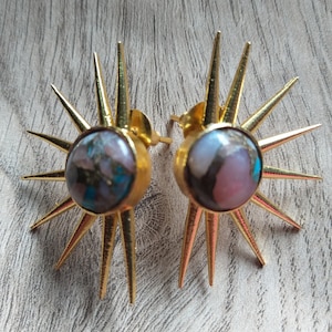 Peut inclure: Une paire de boucles d'oreilles en or avec une pierre rose et bleue sertie au centre de chaque boucle d'oreille. Les boucles d'oreilles ont un design en forme d'étoile avec des pointes acérées.
