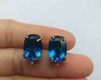 May include: A pair of gold-toned earring findings with blue gemstone accents. The gemstones are rectangular in shape and have a faceted cut.