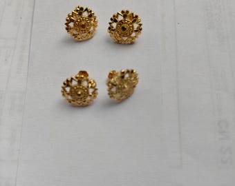 May include: Four gold-colored stud earrings. Each earring features a detailed, floral-like design with a central circular element. The earrings are displayed on a white surface, showcasing their intricate craftsmanship and radiant finish.