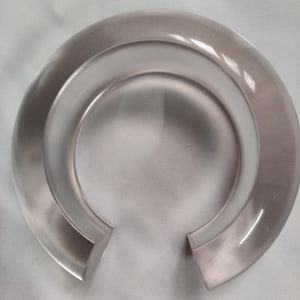 Peut inclure: Un bracelet manchette ouvert et transparent. Le bracelet est de couleur claire et translucide, avec un design circulaire et arrondi. La partie intérieure du bracelet est d'une teinte plus claire, créant un contraste avec la bande extérieure.