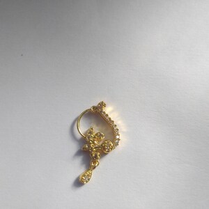 以下が含まれることがあります： 花柄のデザインとクリアなラインストーンが付いた金の鼻のリング。リングはフープの形で、ぶら下がっているドロップがあります。