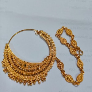 May include: A gold nose ring with a decorative design and a chain attached. The nose ring is made of metal and has a circular shape. The chain is made of small, linked pieces of metal.