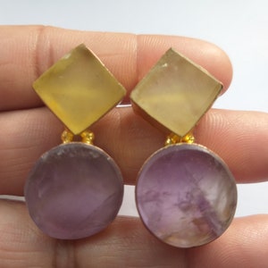 May include: A pair of gold-tone earrings with a square-shaped yellow gemstone and a round purple gemstone.