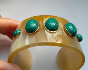 Puede incluir: Un brazalete de cuerno beige con cuatro piedras ovaladas de malaquita verde engastadas en oro.