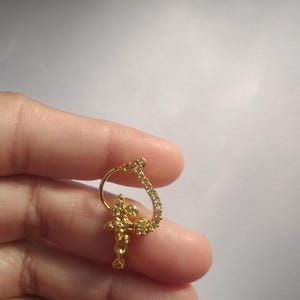 以下が含まれることがあります： 花柄のデザインとクリアなラインストーンが付いたゴールドの鼻のリング