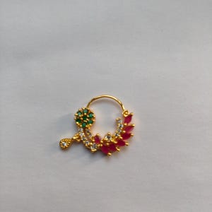 以下が含まれることがあります： 金色のノーズリング、フローラルデザイン。緑と白の石のクラスター、しずく型のチャーム、赤と白の石が特徴です。ジュエリーは白い背景に配置されています。