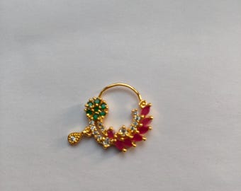 May include: Gold-toned nose ring with a floral design. The ring features a cluster of green and white stones, a teardrop-shaped charm, and a series of red and white stones. The jewelry is set against a white background.