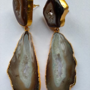 May include: A pair of drop earrings featuring two brown agate slices each, encased in gold-toned metal edges. The top section is a smaller, rounded brown stone, while the bottom section is a larger, elongated, translucent brown agate slice.