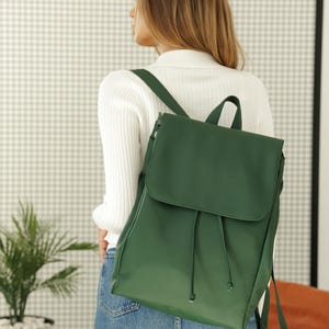 Peut inclure: Un sac à dos vert forêt doté d'un rabat repliable avec fermeture à cordon, de bretelles réglables et d'une poignée supérieure. Le sac présente une finition mate lisse et est porté sur le dos, affichant un design épuré et structuré.