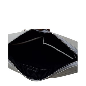 Pu&ograve; includere: Una borsa rettangolare grigio chiaro con cerniera argentata, aperta per rivelare un interno nero. La borsa ha una piccola tasca all'interno. La borsa &egrave; realizzata in un materiale liscio.