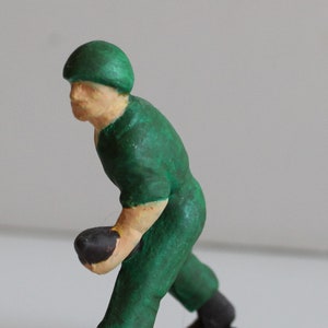 Peut inclure: Une figurine de soldat en plastique vert portant un casque vert et tenant un objet noir dans sa main droite. Le soldat est debout sur une base noire avec une surface texturée.