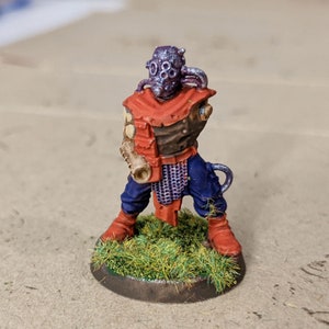 May include: A painted miniature figure of a humanoid with a purple and silver helmet, red and brown armor, and blue pants. The figure is holding a brown weapon and is standing on a green base.
