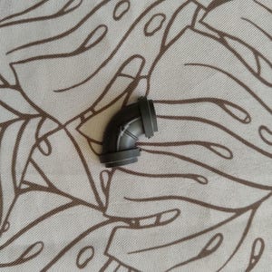 Peut inclure: Raccord de tuyau en plastique noir coudé. Le raccord a un angle de 90 degrés et est conçu pour relier des tuyaux.