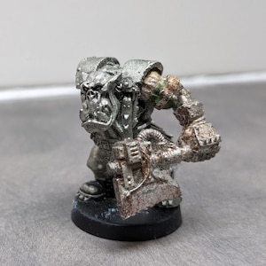 Peut inclure: Une miniature peinte en argent d'un guerrier Orc tenant une grande hache. L'Orc porte une armure et a une expression féroce.