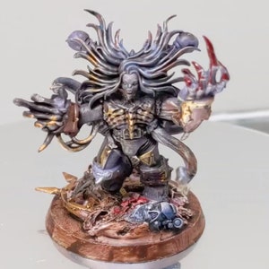 May include: A painted miniature figure of a Chaos Space Marine with a long, flowing mane of hair, multiple arms, and a red claw. The figure is standing on a base with a skull and other debris.