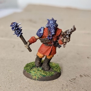 May include: A miniature figure of a soldier wearing a purple and silver helmet with a gas mask, a red and orange uniform, and holding a spiked club and a gun. The figure is standing on a green base.