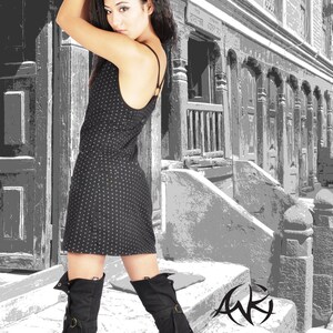 Può includere: Una donna indossa un abito a pois neri e bianchi e stivali neri alti fino al ginocchio, in piedi davanti a un edificio con una facciata a motivi in bianco e nero.