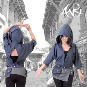 Könnte beinhalten: Zwei Frauen tragen blaue Kapuzenpullover mit einem grauen und schwarzen Gürtel. Die Pullover haben einen Knoten in der Taille und einen Ausschnitt im Rücken. Die Frauen stehen vor einem grauen und weißen Gebäude.