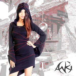 Könnte beinhalten: Ein schwarzes Kapuzenkleid mit roten Nähten und langen Ärmeln. Das Kleid hat ein tailliertes Oberteil und einen fließenden Rock. Das Model steht vor einem Backsteingebäude mit einem Schild, auf dem "Shri Narayan Temple" steht.
