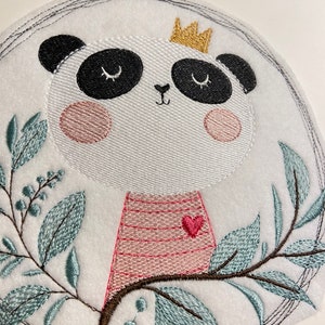 Könnte beinhalten: Gestickter Aufnäher mit einem niedlichen Panda, der eine Krone und ein rosa gestreiftes Hemd mit einem Herzen trägt. Der Panda ist von grünen Blättern und Beeren umgeben.