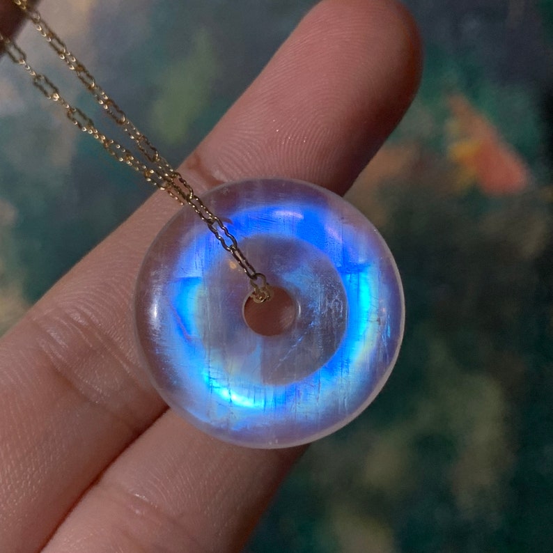 May include: A white iridescent moonstone pendant in the shape of a donut, with a gold chain.