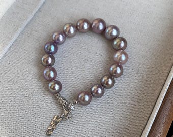 May include: A pearl bracelet with a silver charm. The pearls are a mix of purple and gray.