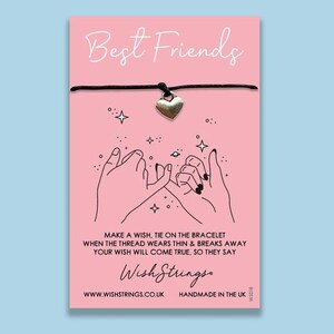 May include: Pink card with the text "Best Friends" and a black string bracelet with a silver heart charm. The card also has a black and white illustration of two hands intertwined with the text "Make a wish, tie on the bracelet when the thread wears thin & breaks away your wish will come true, so they say." The card also has the text "Wish Strings" and "www.wishstrings.co.uk Handmade in the UK."